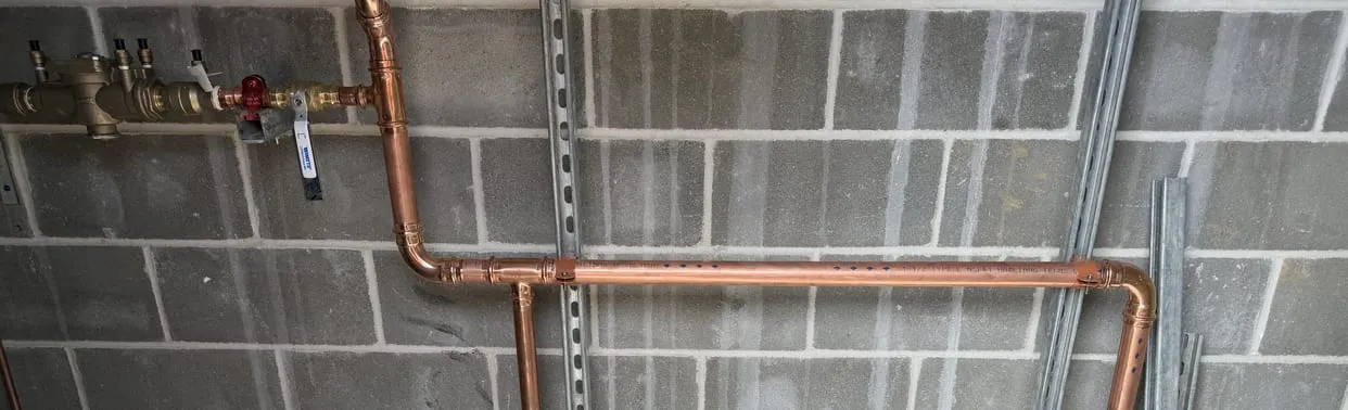 Copper water lines and a backflow assembly installed on a block wall