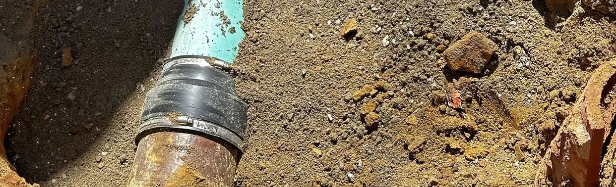 New PVC sewer pipe joined to the old cast-iron line with a rubber coupling in an open trench
