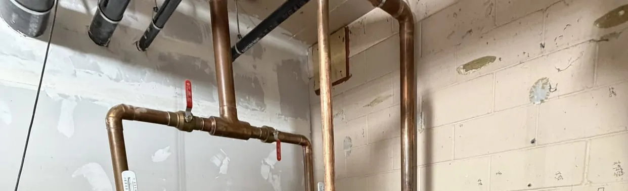 Copper hot and cold lines and a shutoff valve on a basement wall
